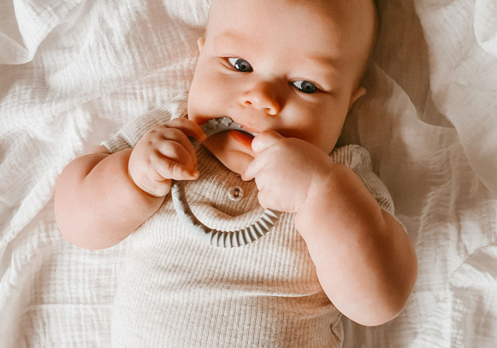 baby lying on a soft blanket, chewing teething ring