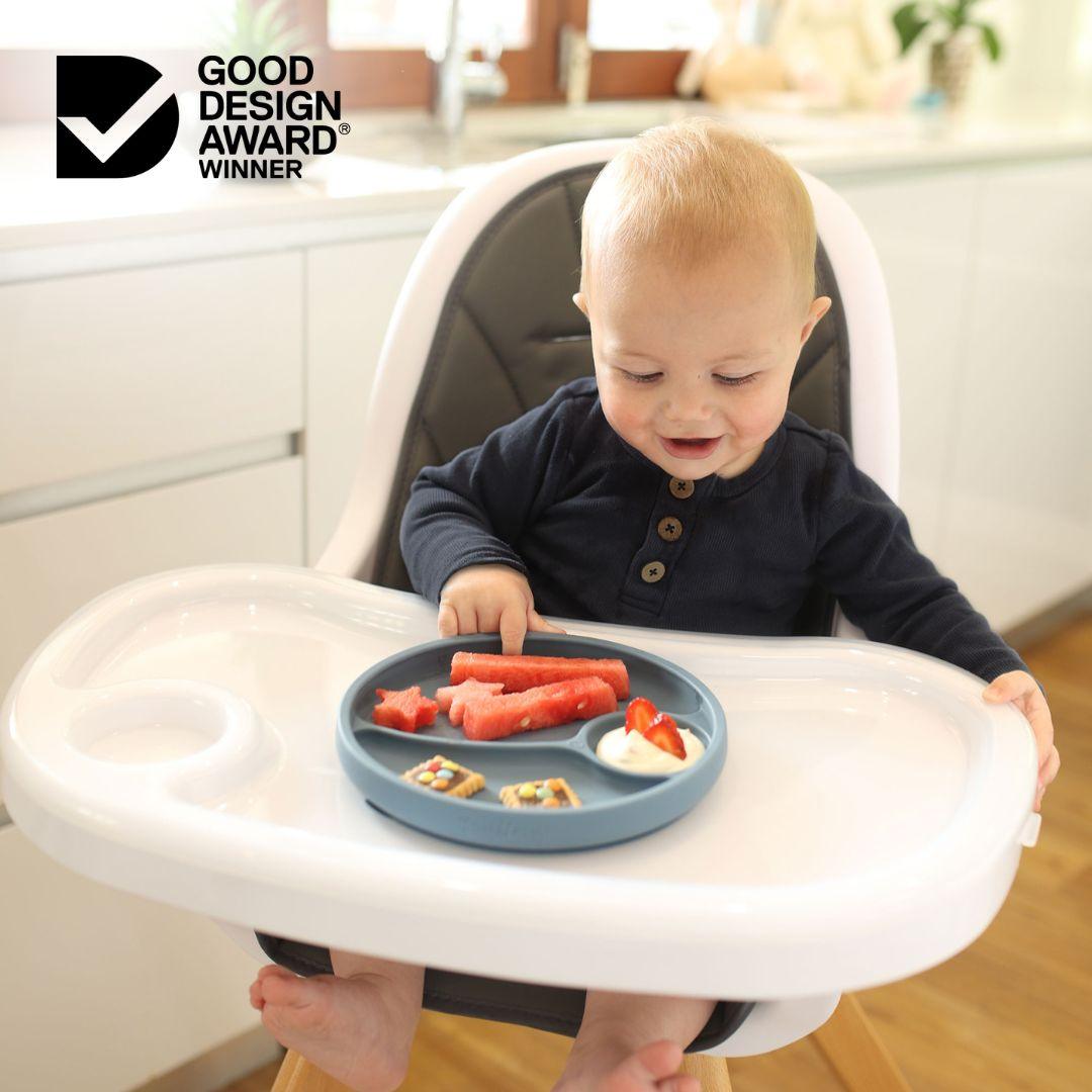 baby boy sitting in a high char eating food from divided suction plate 