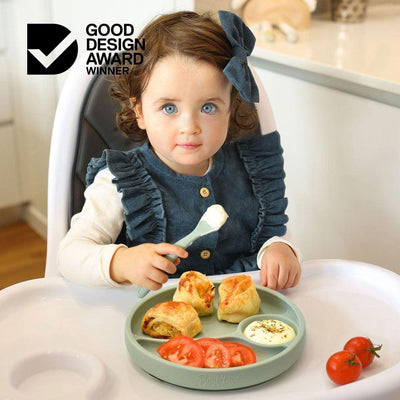 toddler girl eating lunch from a divided suction plate sitting in a high chair
