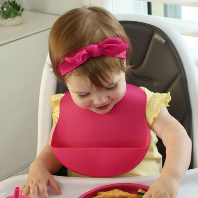 Toddler Girl sitting in a high chair eating dinner and wearing a hot pink silicone bib