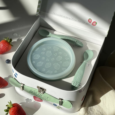 Children's tableware set with bowl, lid and spoons in a keepsake gift box, surrounded by strawberries.
