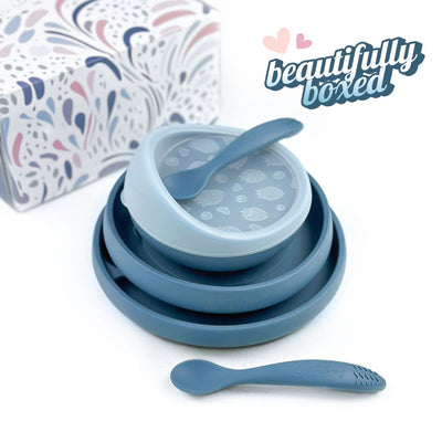 Brightberry self-feeding set for babies in a blue colourway, featuring a suction bowl with lid and spoon, easy-scooping plate, and ergonomic training spoon, all neatly stacked beside a beautifully patterned gift box. Text overlay reads “Beautifully boxed” with decorative heart graphics.