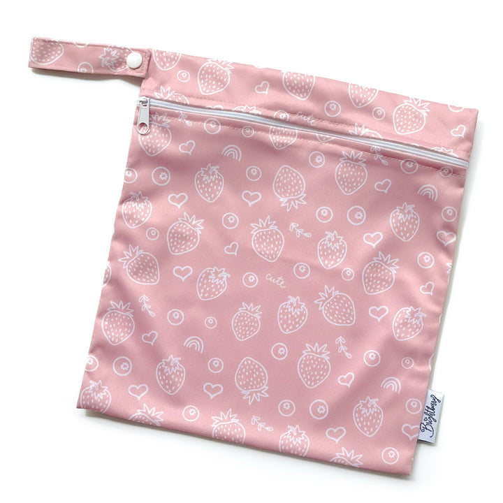 Coral pink waterproof bag with white strawberry print, zip closure and snap-button carry handle.