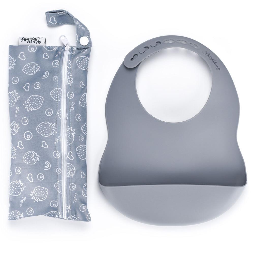 A sleek slate-colored silicone pocket bib, easily rolled for compact storage, displayed next to its waterproof carry bag with a zipper and handle, ideal for dining out or quick meals away from home.