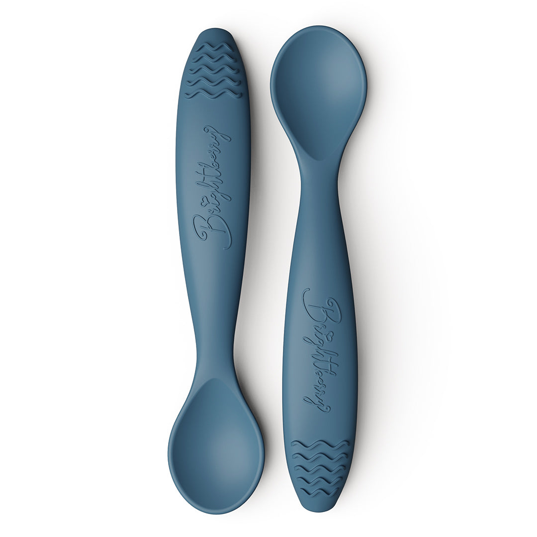Two blueberry navy blue baby spoons with textured teething handles on a white background.