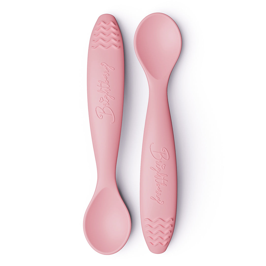 Two coral pink baby spoons with textured teething handles on a white background.