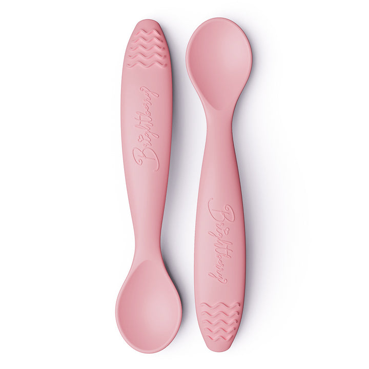 Two coral pink baby spoons with textured teething handles on a white background.