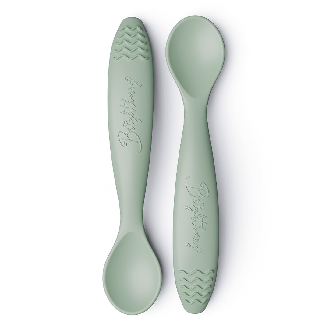 Two sage green baby spoons with textured teething handles on a white background.