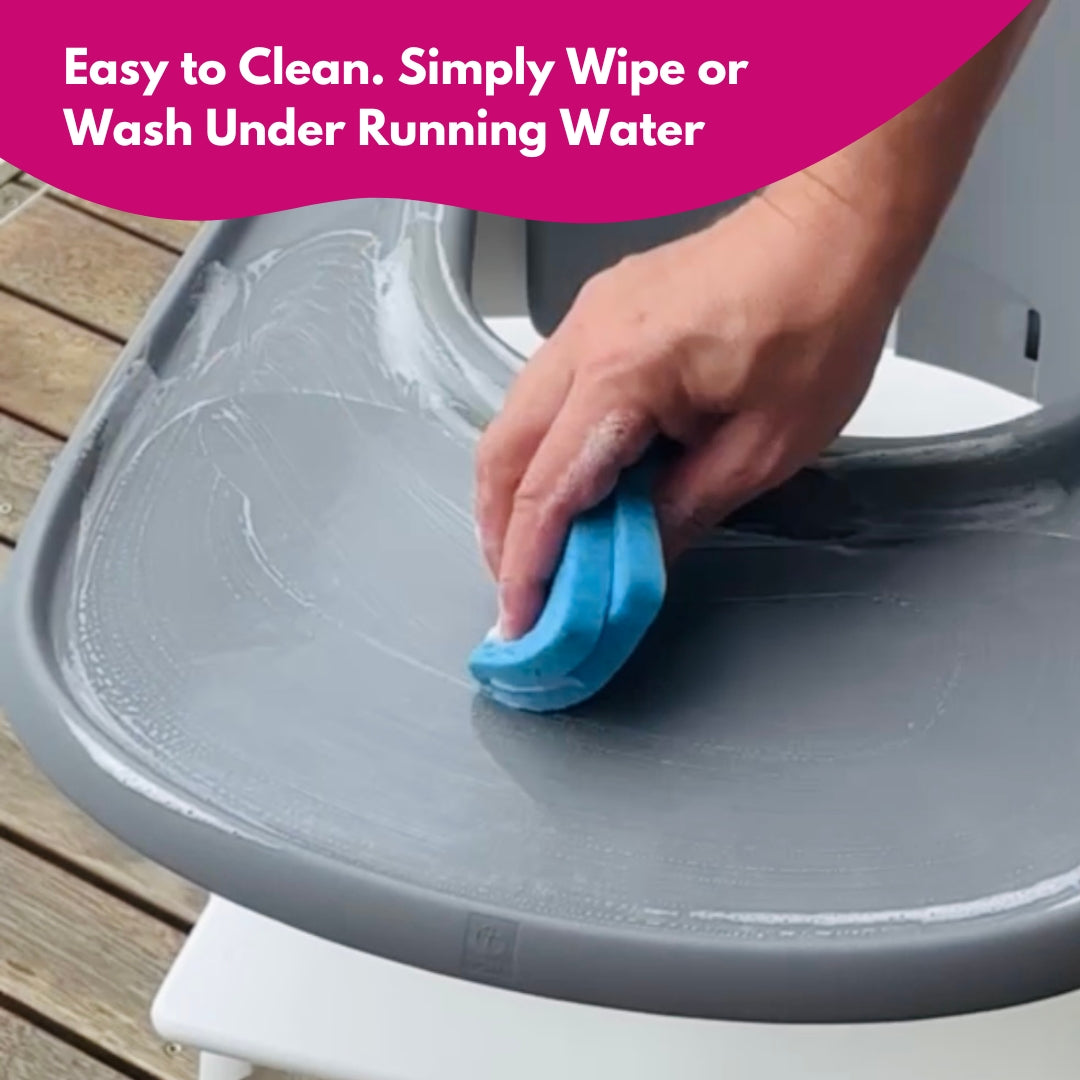 Wiping high chair tray with suction sticker using sponge under running water for easy cleaning