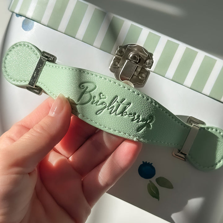 Hand holding a green strap with 'Brightberry' branding - showing product packaging detail.