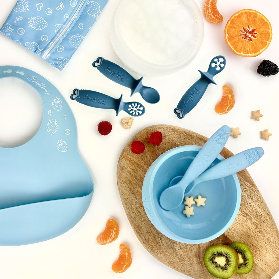 Starting Solids Set in Pacific with silicone suction bowl, lid, bib, waterproof bag, two theOne spoons and theFirst baby spoons in Blueberry