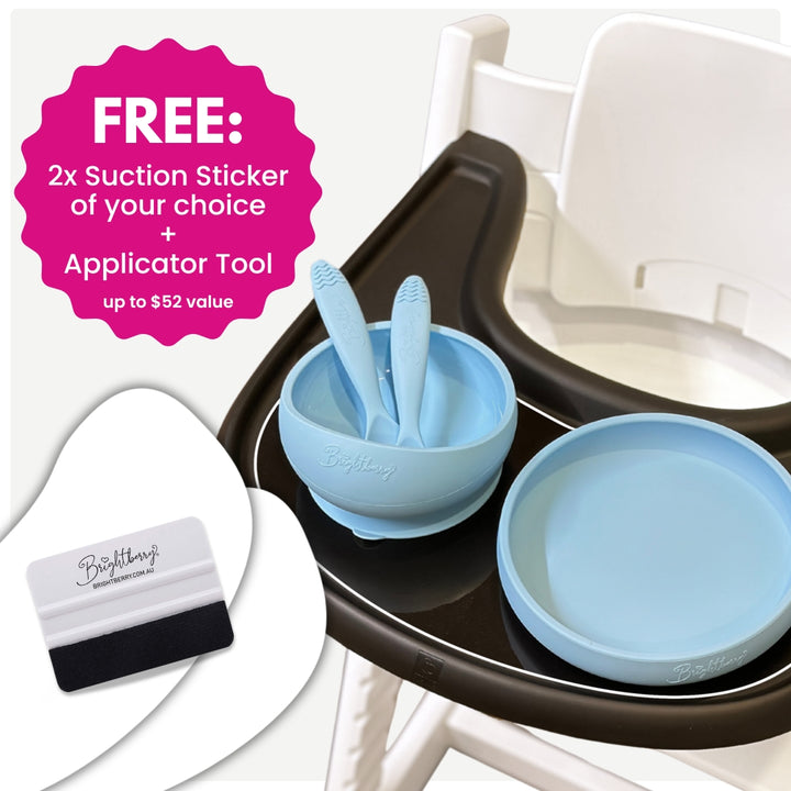 Brightberry suction bowl and plate set in light blue on a high chair tray, with two ergonomic spoons inside the bowl. Overlay text highlights a special offer: free 2x suction stickers of your choice and a free sticker applicator tool, valued at over $50.