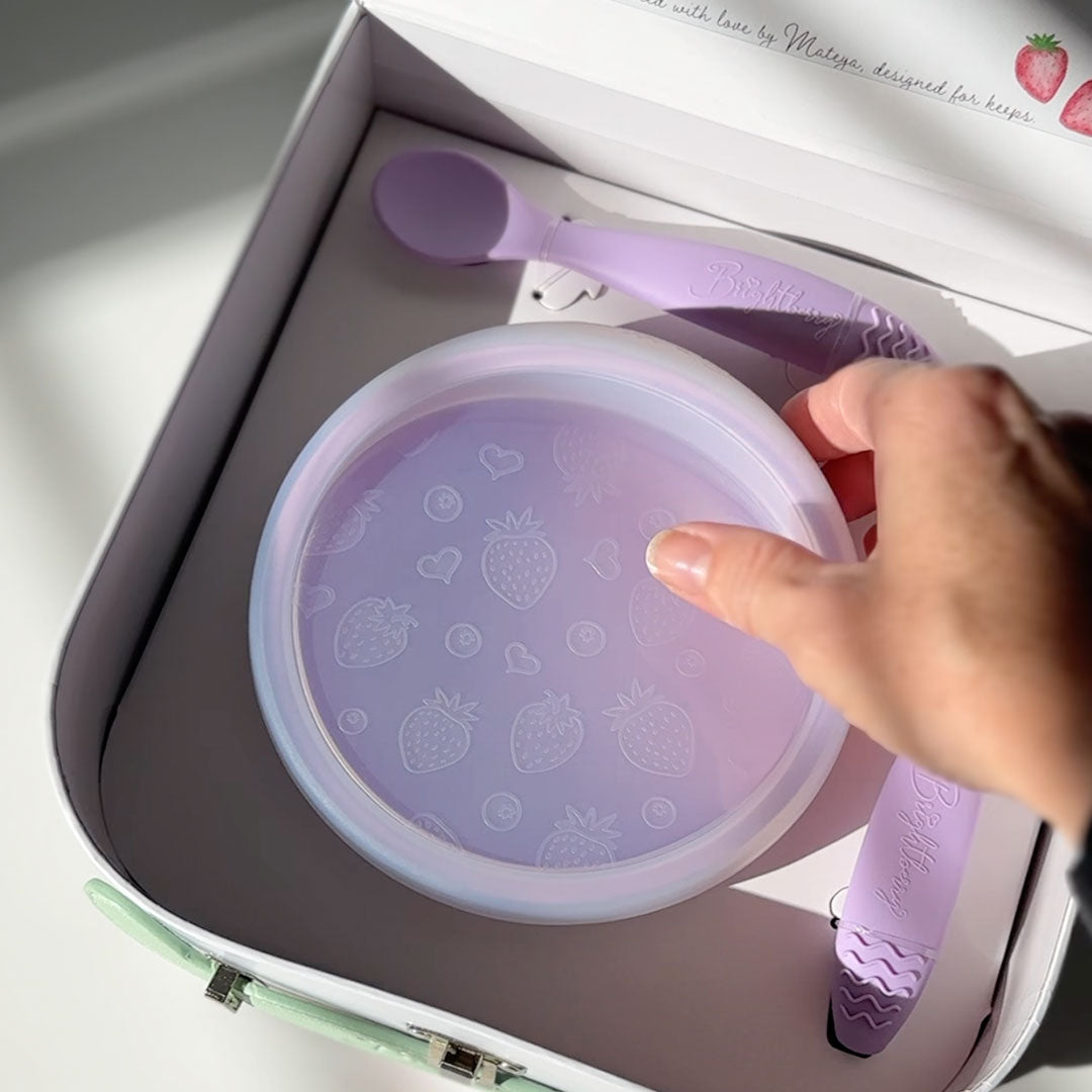 Hand uUnboxing purple children's bowl with lid and spoons set packed in a premium baby gift box.