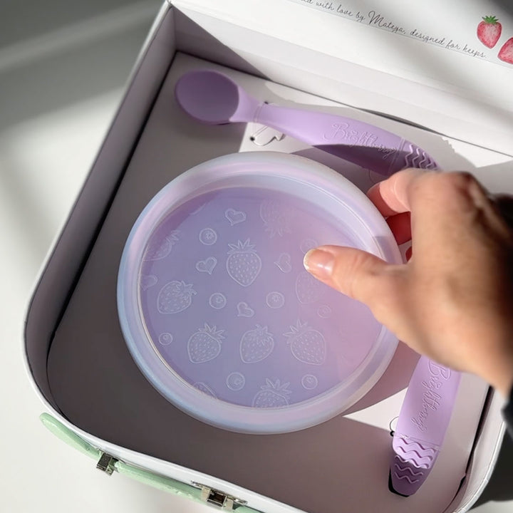 Hand uUnboxing purple children's bowl with lid and spoons set packed in a premium baby gift box.