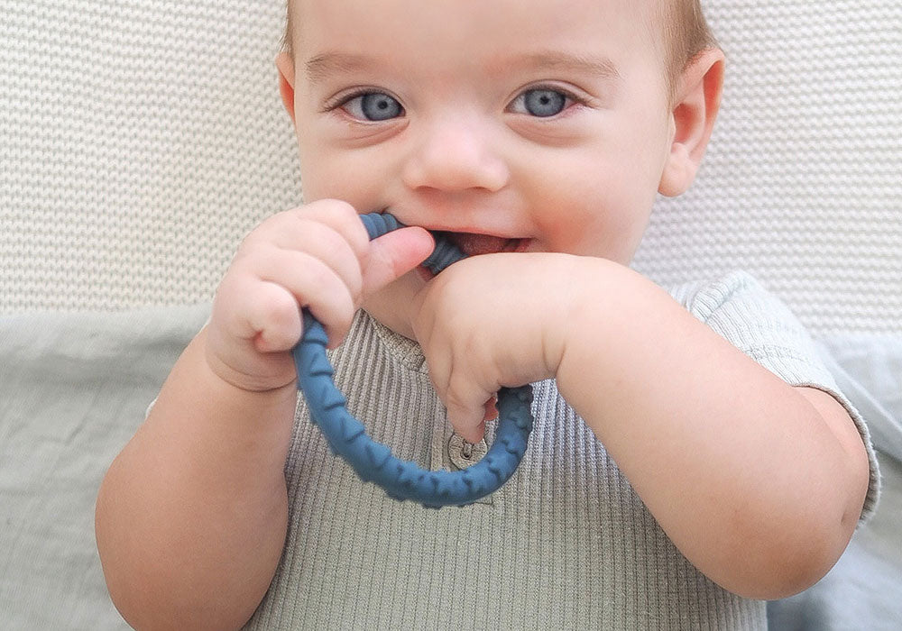 teething baby boy smiling and chewing on teether ring toy